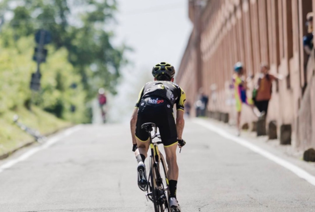 Ciclista professionista Simon Yates in salita visto di spalle sul San Luca